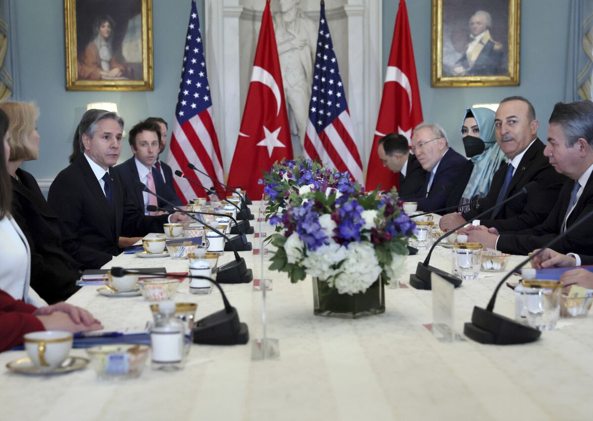 Diplomats sit across a long table from each other, with Turkish and U.S. flags in the background