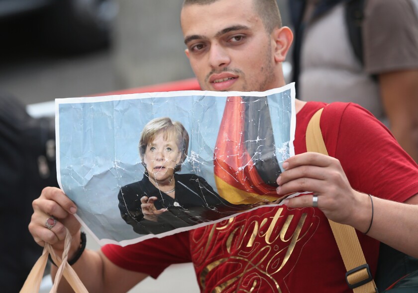 A migrant from Syria holds a picture of German Chancellor Angela Merkel as he arrives from Hungary at Munich's main railway station on Sept. 5. Germany has agreed to set aside more than $6 billion next year to help migrants.