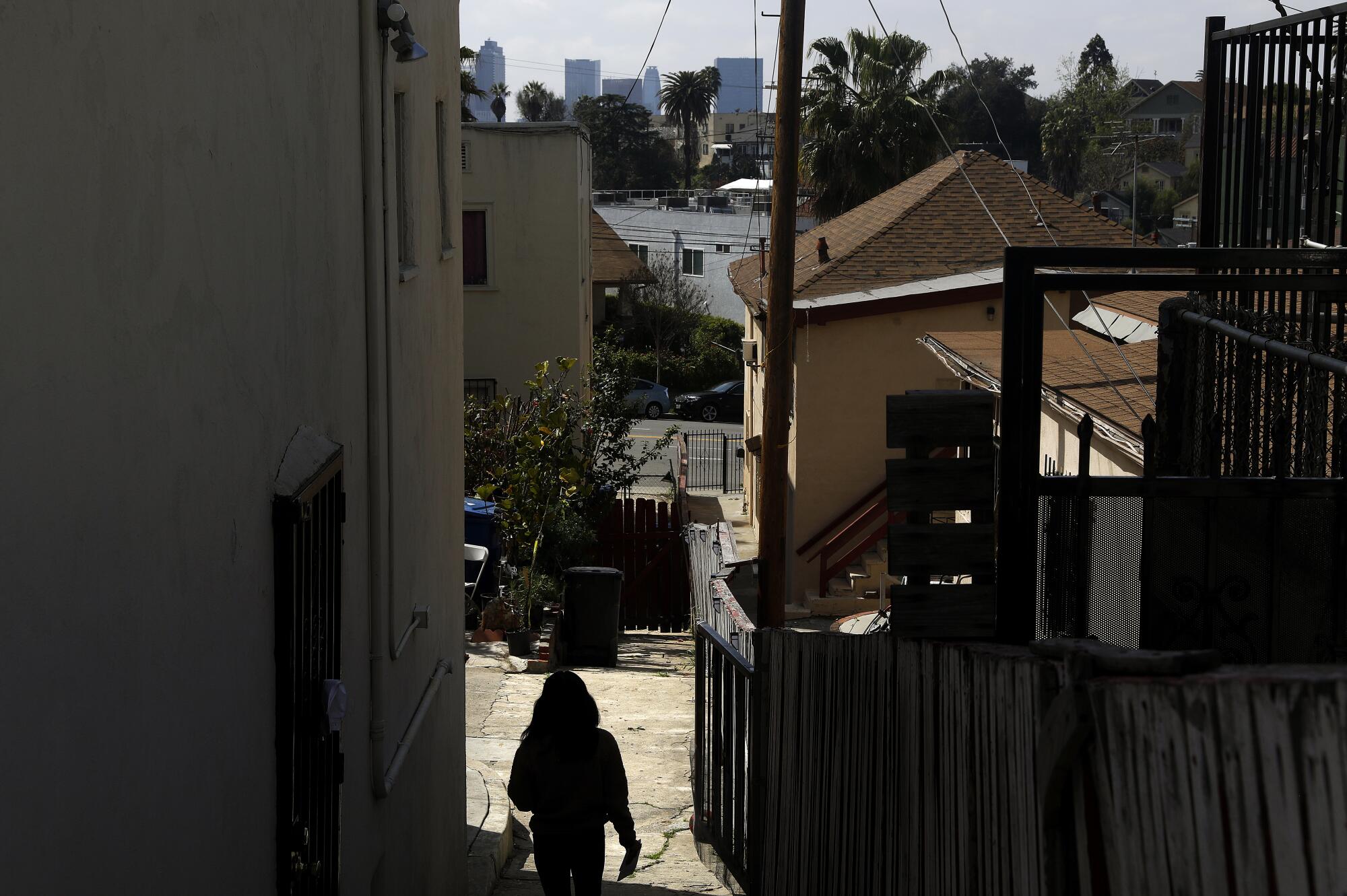 A person walks next to an apartment complex with a view of downtown L.A. in the distance. 