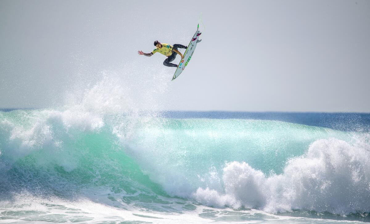 A surfer flies above a crashing blue wave