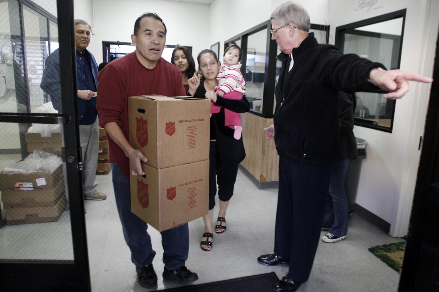 Rafael Fernandez, from second left, carries boxes of food for Jane, 12, Lucy and Roselyn Vasquez while Major Bob Rudd directs them to go outside during a Christmas distribution that took place at the Salvation Army in Burbank on Thursday, December 15, 2011. The Salvation Army is expecting over 1200 people during the distribution.