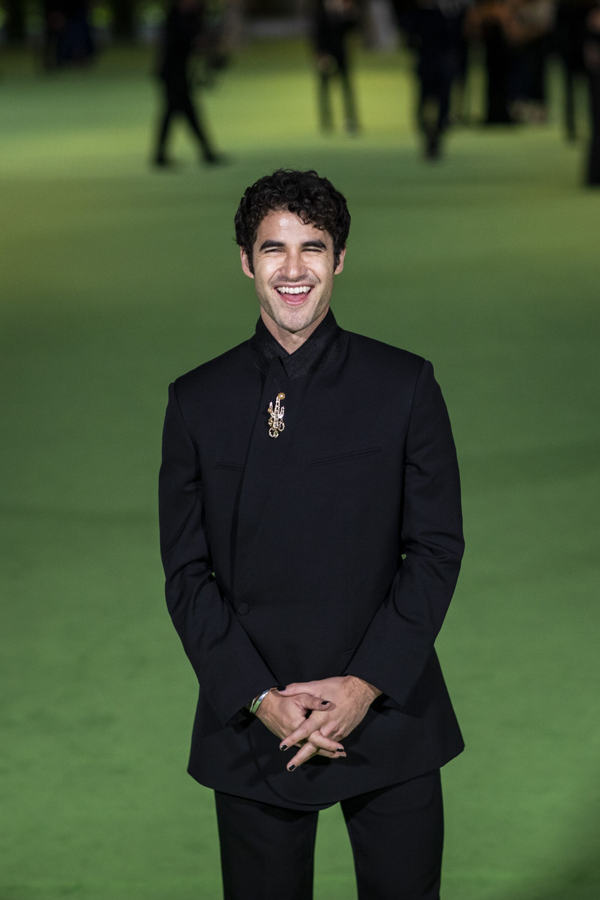 A man smiling in a black suit on a green carpet