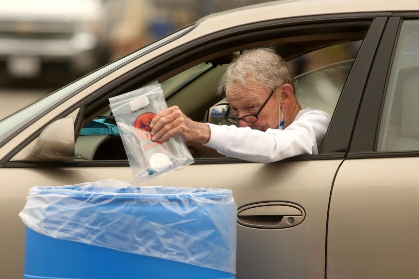 LOS ANGELES, CA - APRIL 07, 2020 - - A man drops off his self-administered COVID-19 test in a blue bin at a drive-up test site at the Veterans Administration Parking Lot 15 outside of Jackie Robinson Stadium in Los Angeles on April 7, 2020. The test site is located at 100 Constitution Avenue on the VA campus. The tests are self-administered, and people are instructed on how to swab their own mouths/throats when they arrive. Those who are interested in being tested must register ahead of time at coronavirus.lacity.org/testing. Walk-up appointments are not offered. (Genaro Molina / Los Angeles Times)