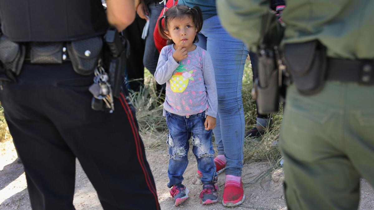 A police officer and a Border Patrol agent watch over a group of Central American asylum seekers before taking them into custody on June 12, 2018 near McAllen, Texas.