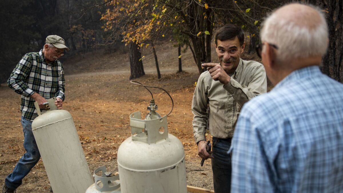 Jeff Evans, center, chats with his dad, Chuck, as neighbor Gary Green moves propane tanks Friday in Concow, Calif. (Kent Nishimura / Los Angeles Times)