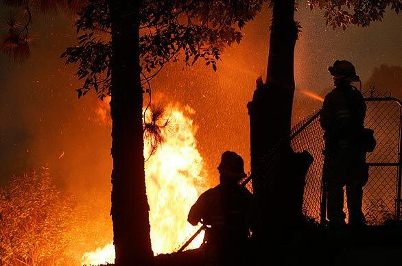 Capt. Scott Herring, left, keeps an eye on the flames as firefighter Jason Watkins keeps the trees wet in the backyard of a home in the 3000 block of Hopeton Road in La Crescenta.
