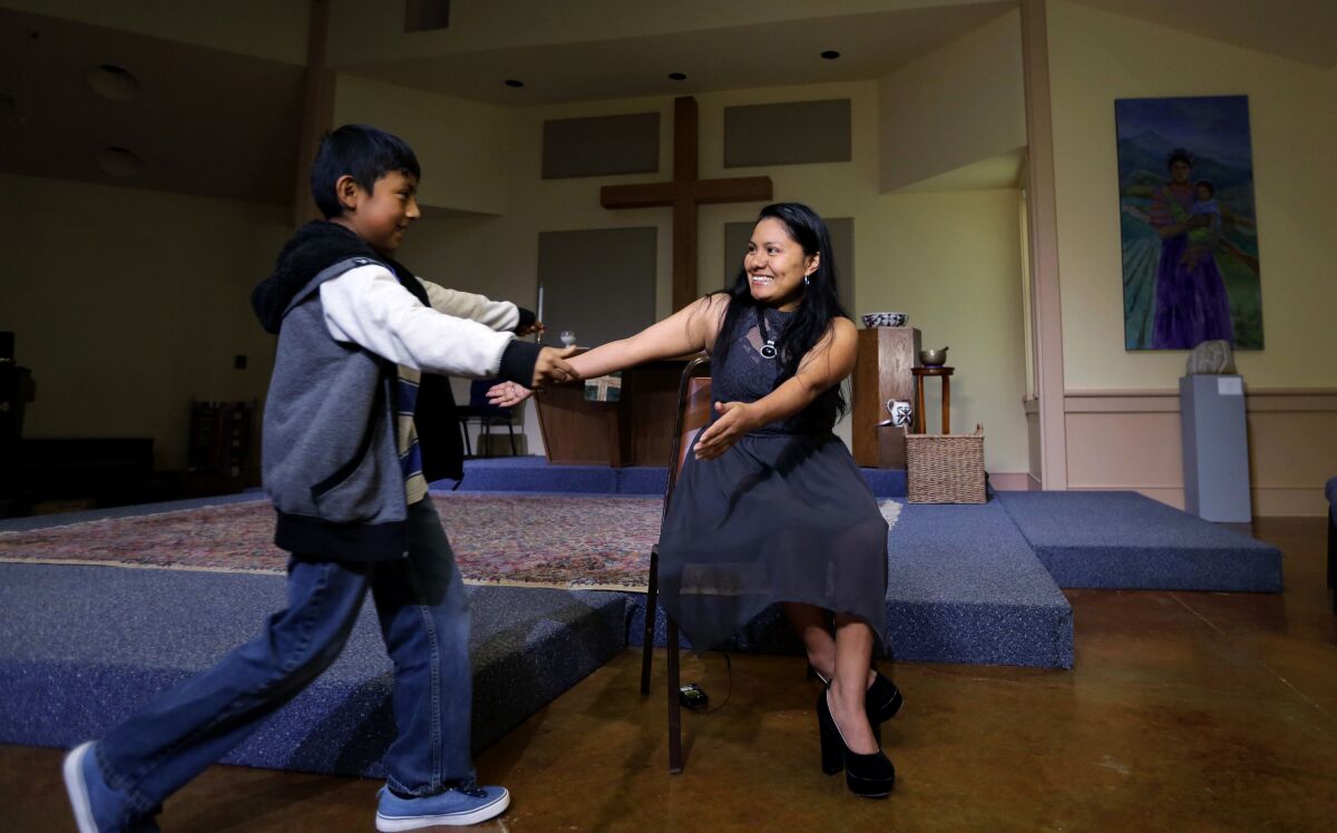 A woman and boy, inside a church, reach out their arms to each other.