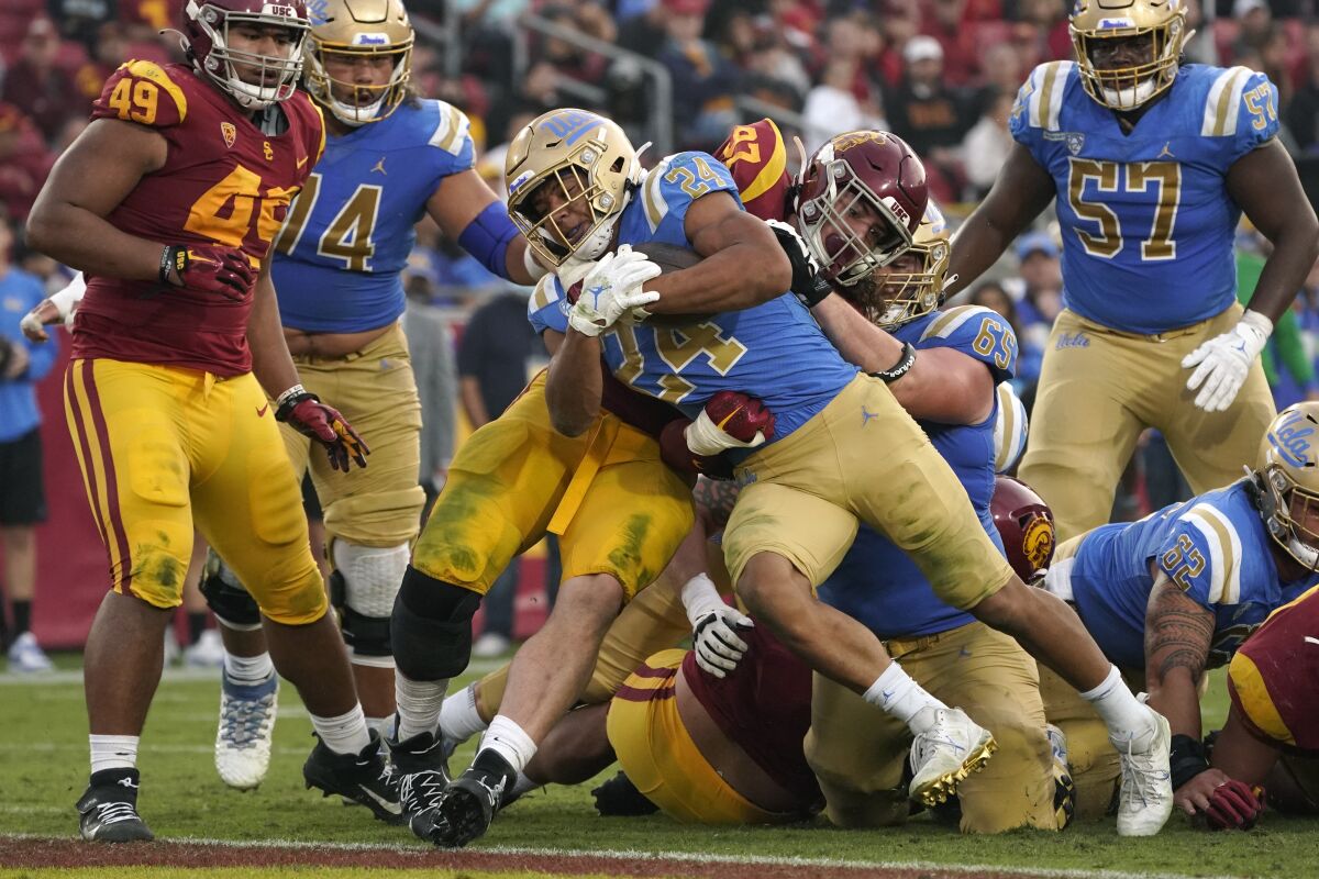 FILE - UCLA running back Zach Charbonnet (24) runs the ball in for a touch down as Southern California defensive lineman Jacob Lichtenstein (97) tries to stop him during the second half of an NCAA college football game Saturday, Nov. 20, 2021, in Los Angeles. An advocacy group for college athletes has filed a complaint with the National Labor Relations board in the next step in a push to give employee status to college athletes and afford them the right to competitive pay, collective bargaining and other benefits and protections. The National College Players Association on Tuesday, Feb. 8, 2022 filed the unfair labor practice charges against the NCAA, Pac-12 Conference, UCLA and the University of Southern California (AP Photo/Mark J. Terrill, File)