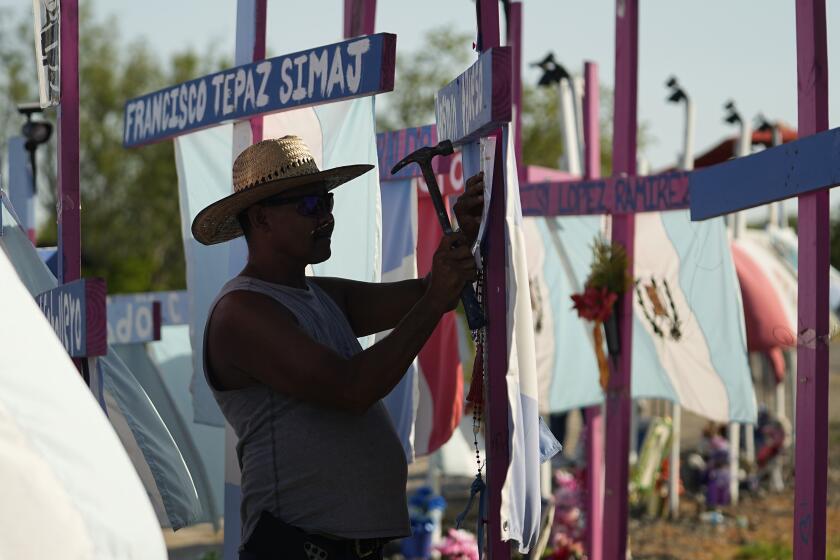 Christian Rodriguez tacks a poem to a cross that is part of a makeshift memorial at the site where officials found dozens of people dead in an abandoned semitrailer containing suspected migrants last summer, Tuesday, June 27, 2023, in San Antonio. U.S. authorities announced the arrests of four more people in connection to the smuggling deaths of 53 migrants, including eight children, who were left in a tractor trailer in the scorching Texas summer. (AP Photo/Eric Gay)