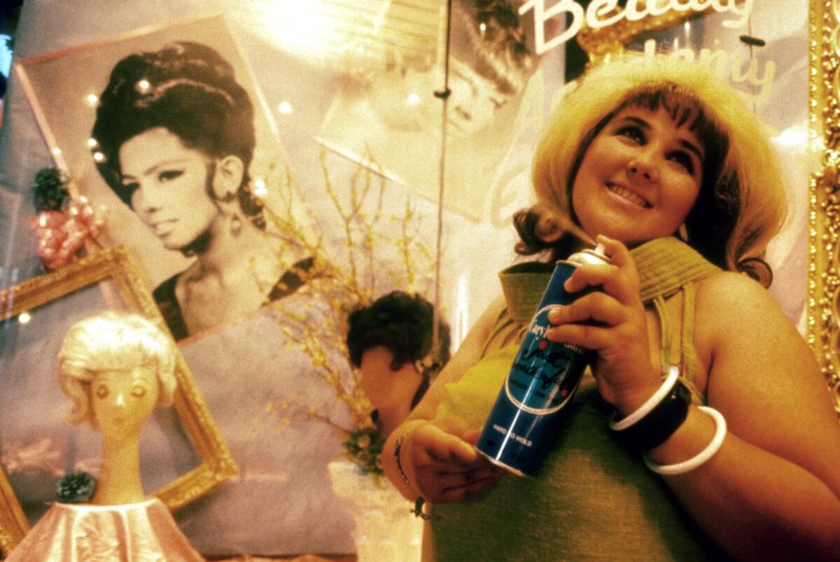 A woman holding a hairspray can in front of a designed wall