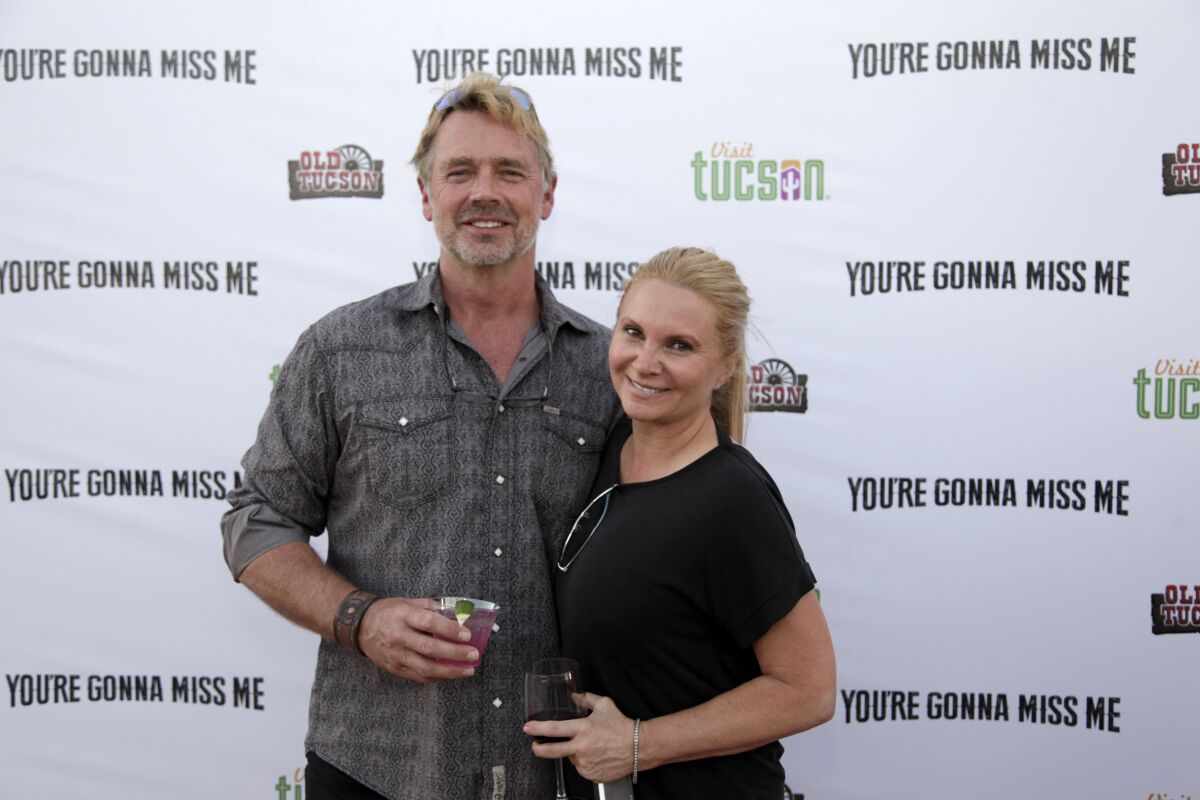 A man with short gray hair and a beard smiling and posing with a woman with long blond hair. Both are holding drinks