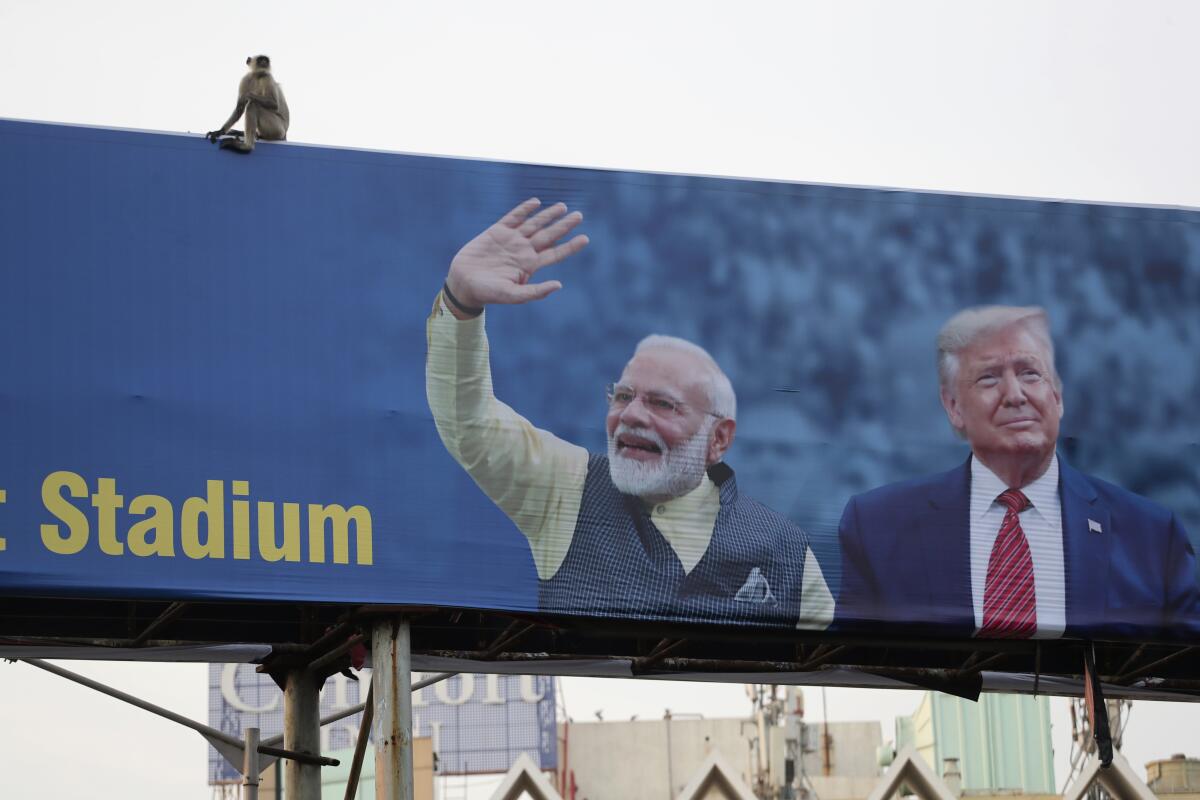 A monkey sits on a billboard featuring Indian Prime Minister Narendra Modi, left, and President Trump.