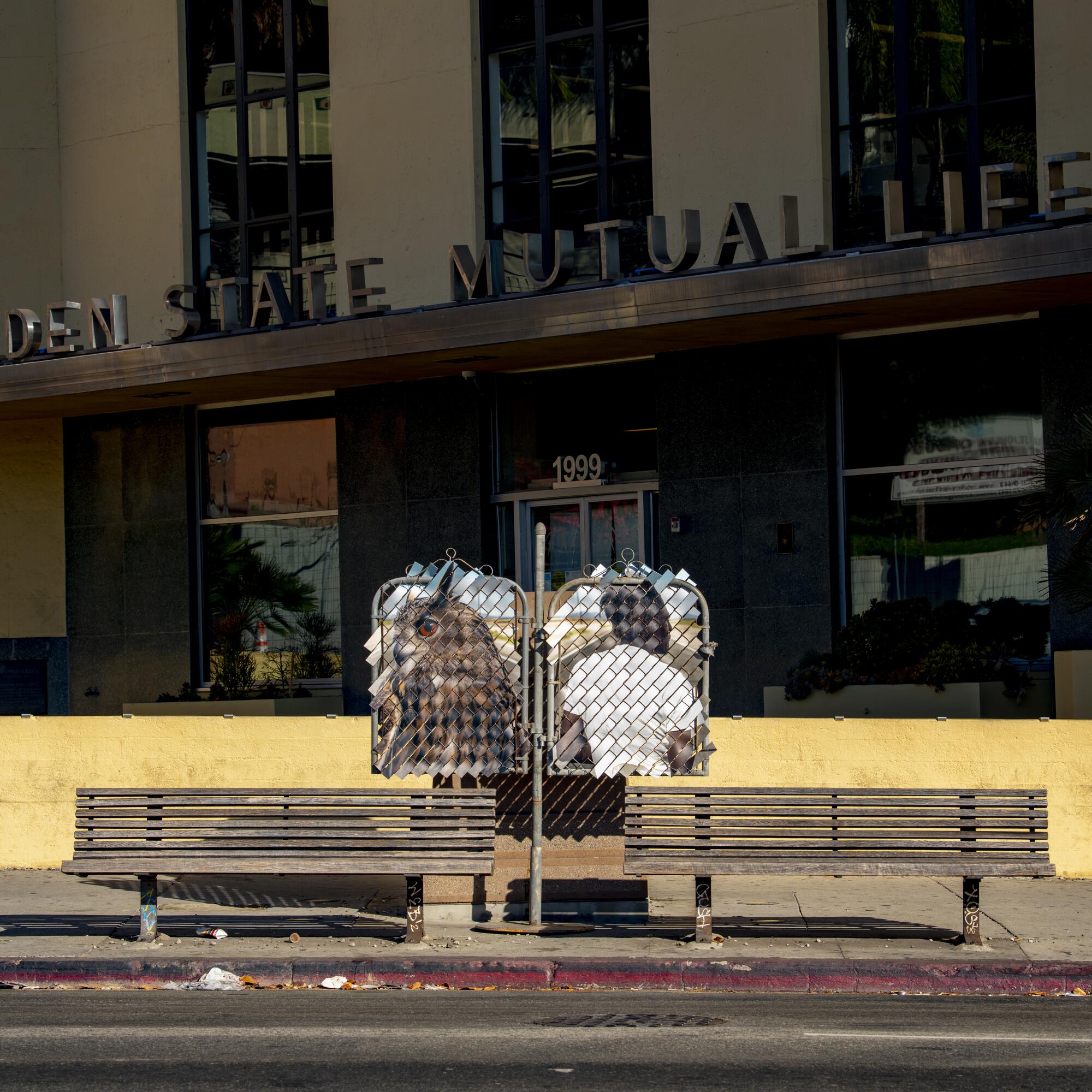 Two portraits on either side of a pole sit between benches in front of a building.