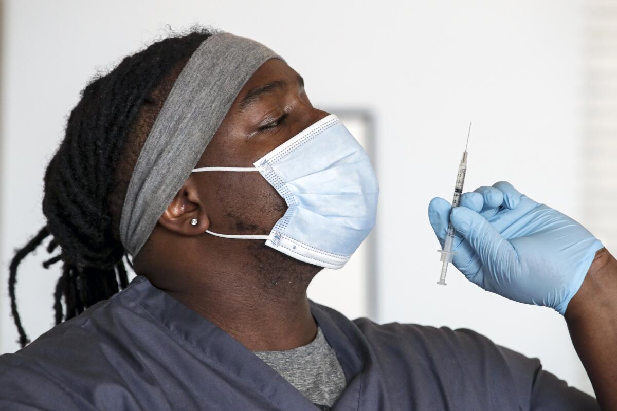 Medical assistant Adrian Davis checks for air-bubbles in a syringe before giving a COVID-19 vaccine. 