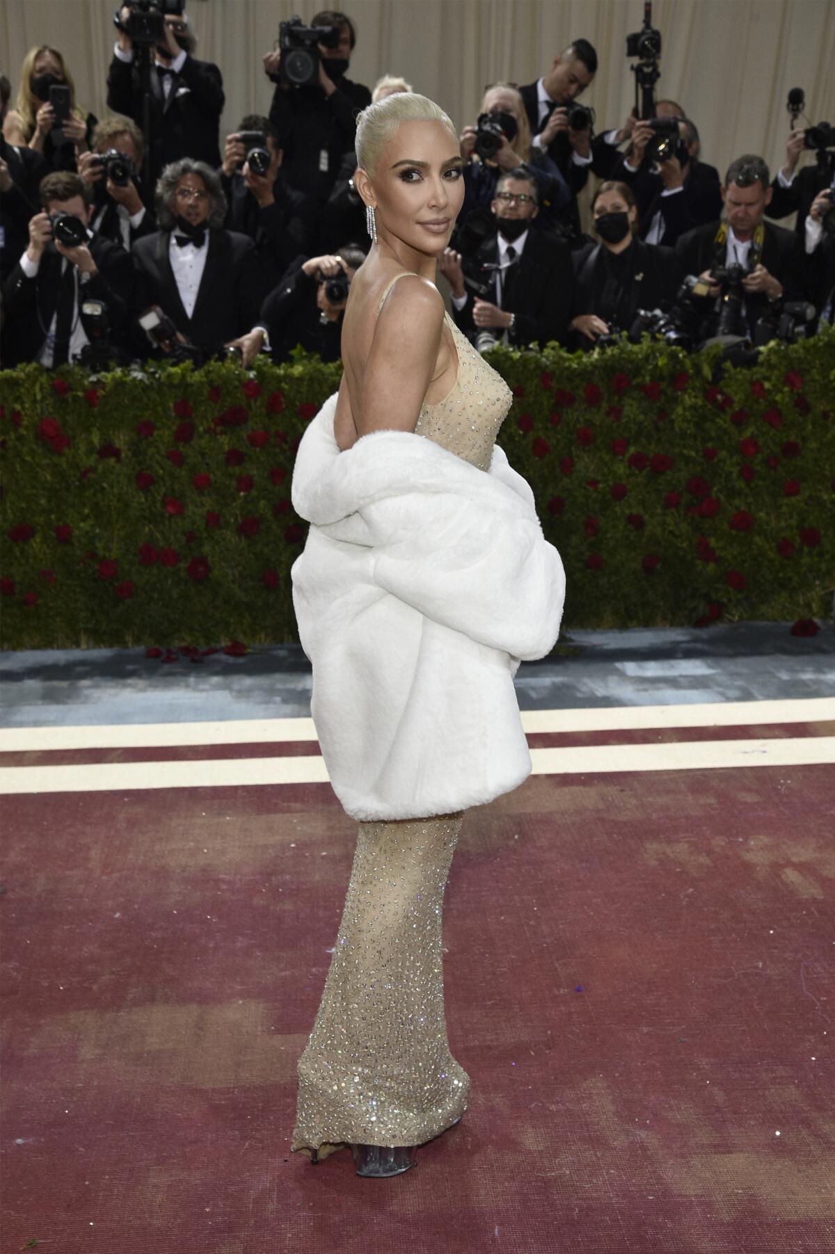 A woman poses in a nude-color gown and a white fur stole 