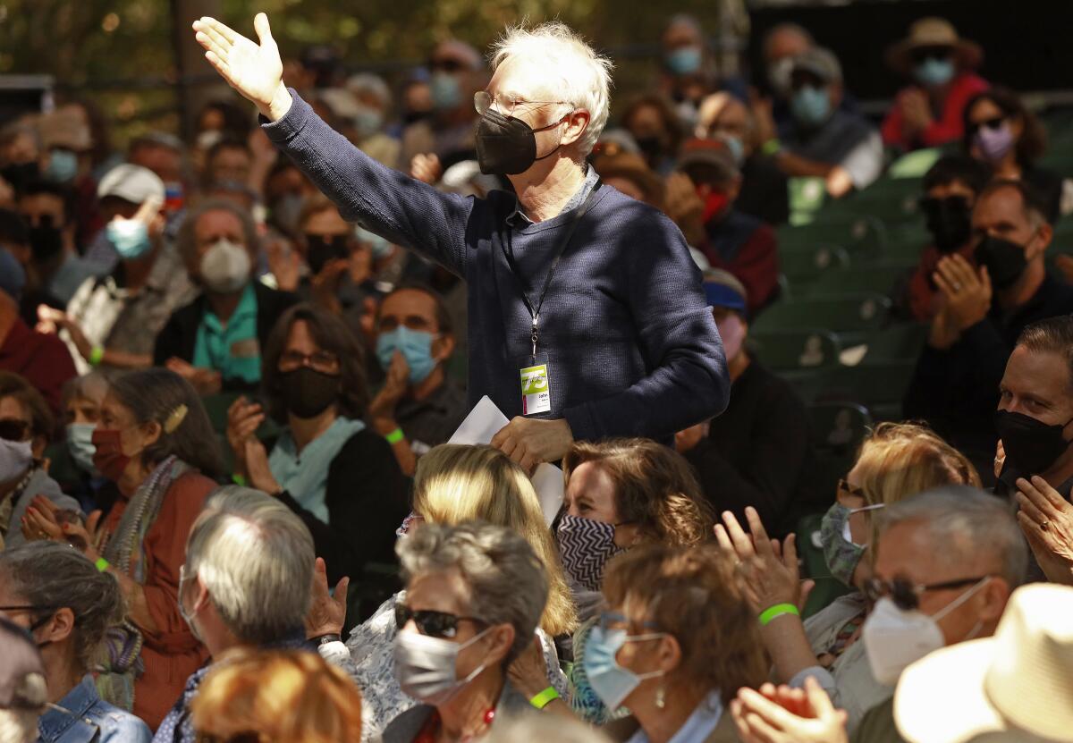 A man stands in a seated crowd and raises his arm