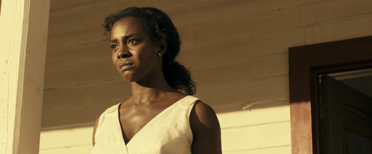 A woman in a white dress frowning on her front porch