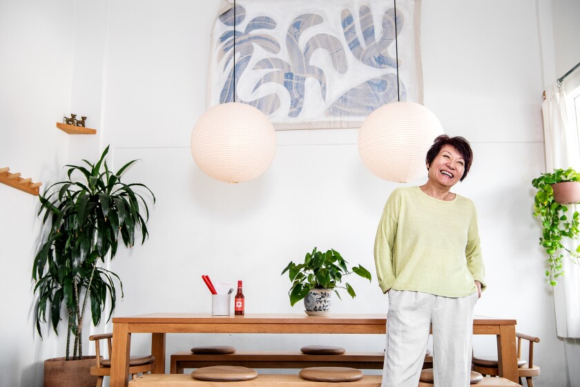 A woman stands with her hands in her pockets, smiling.
