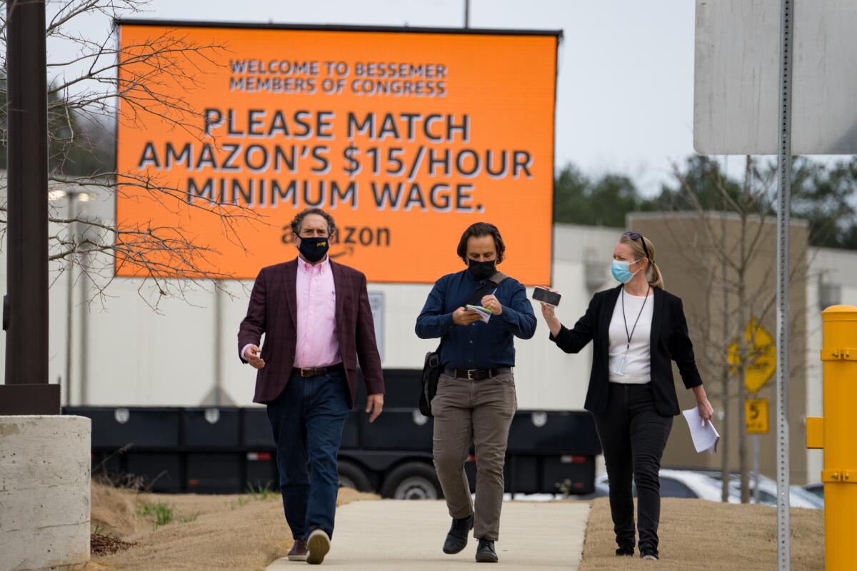 Congress members walk beneath a sign that says "Please match Amazon's $15/hour minimum wage."