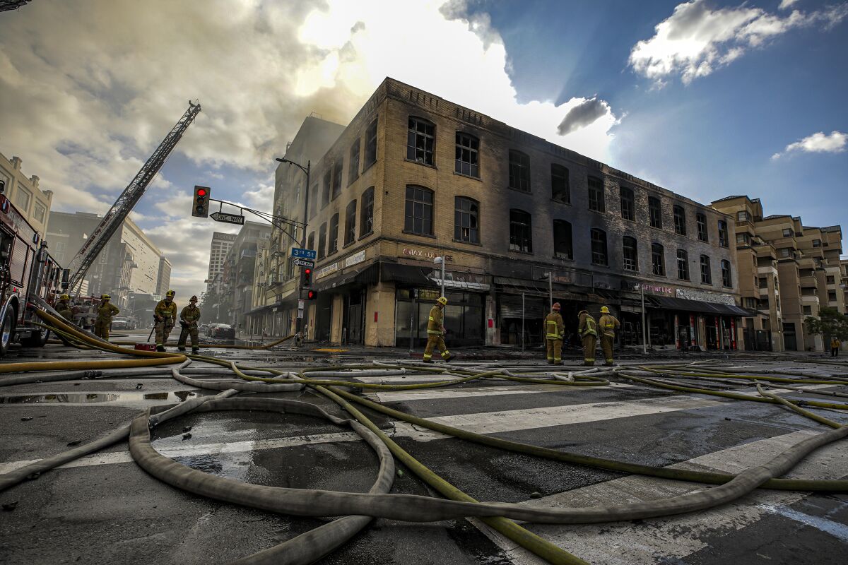 Firehoses criss-cross the street in front of a burned out three-story commercial building