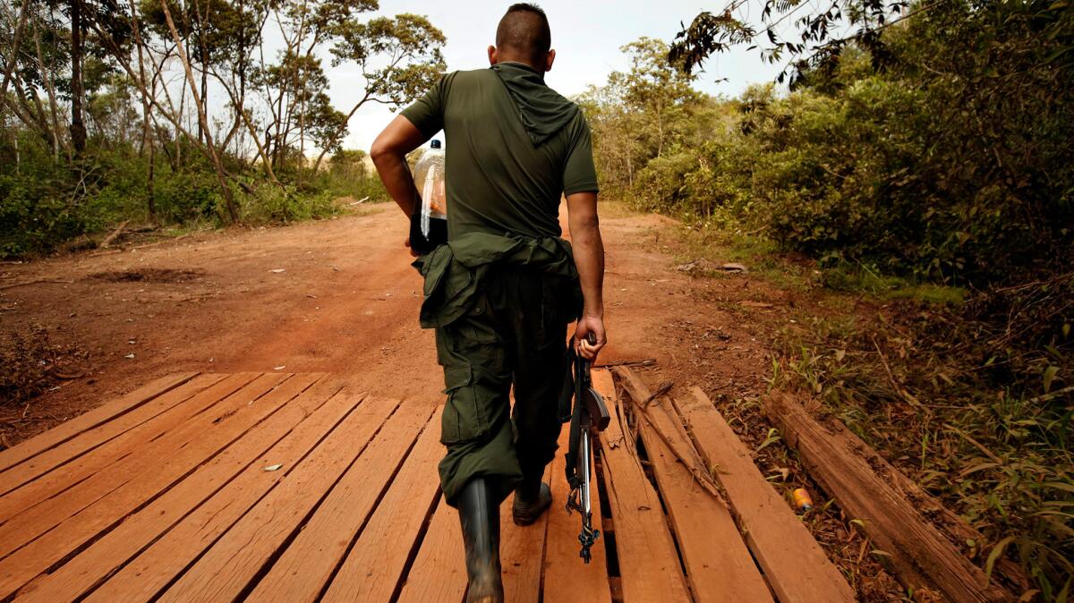 A FARC member carries his weapon along with a bottle of soda, as he leaves camp.