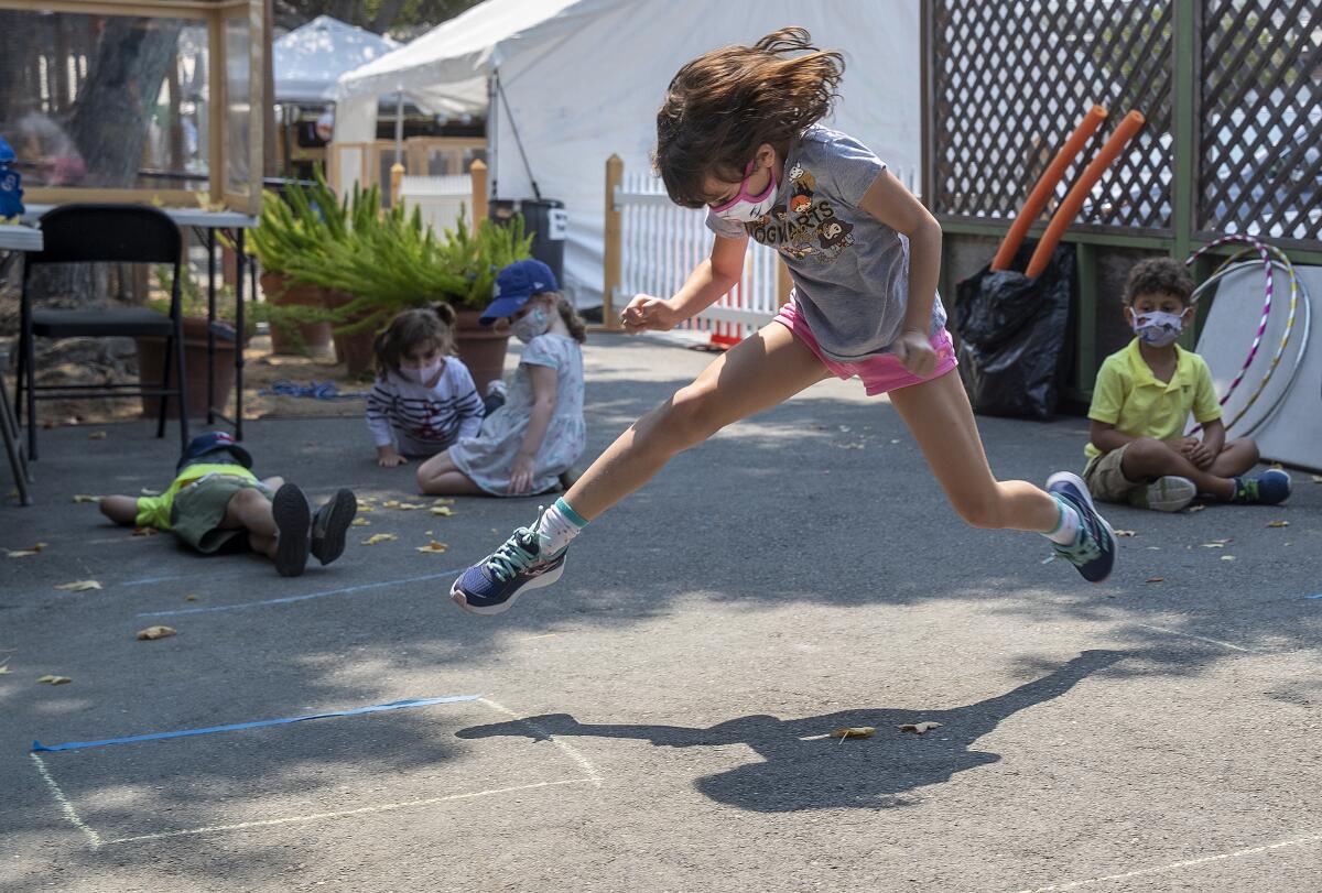 A third-grader jumps from one chalk lined box to the next while playing a game with schoolmates, all of them in masks.