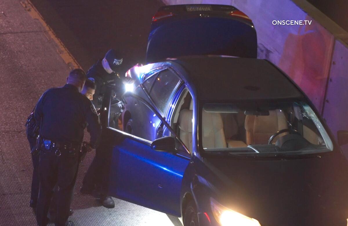 Police officers search a car with its trunk and doors open
