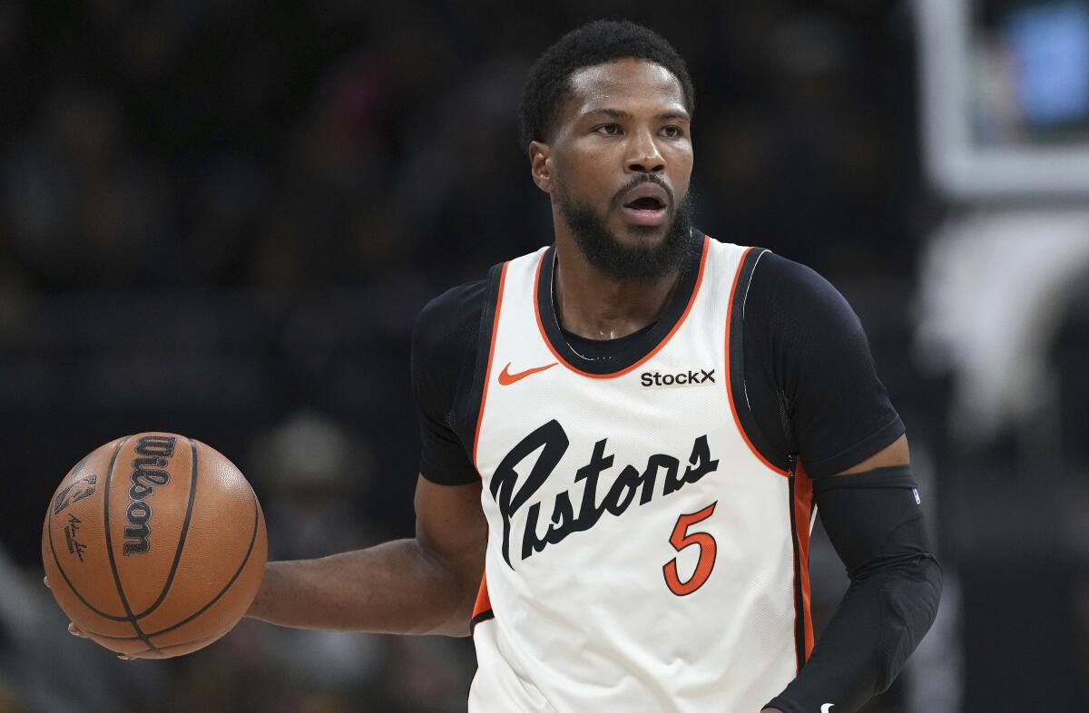 Malik Beasley wearing jersey number 5 over a T-shirt and an arm sleeve moves the ball up court