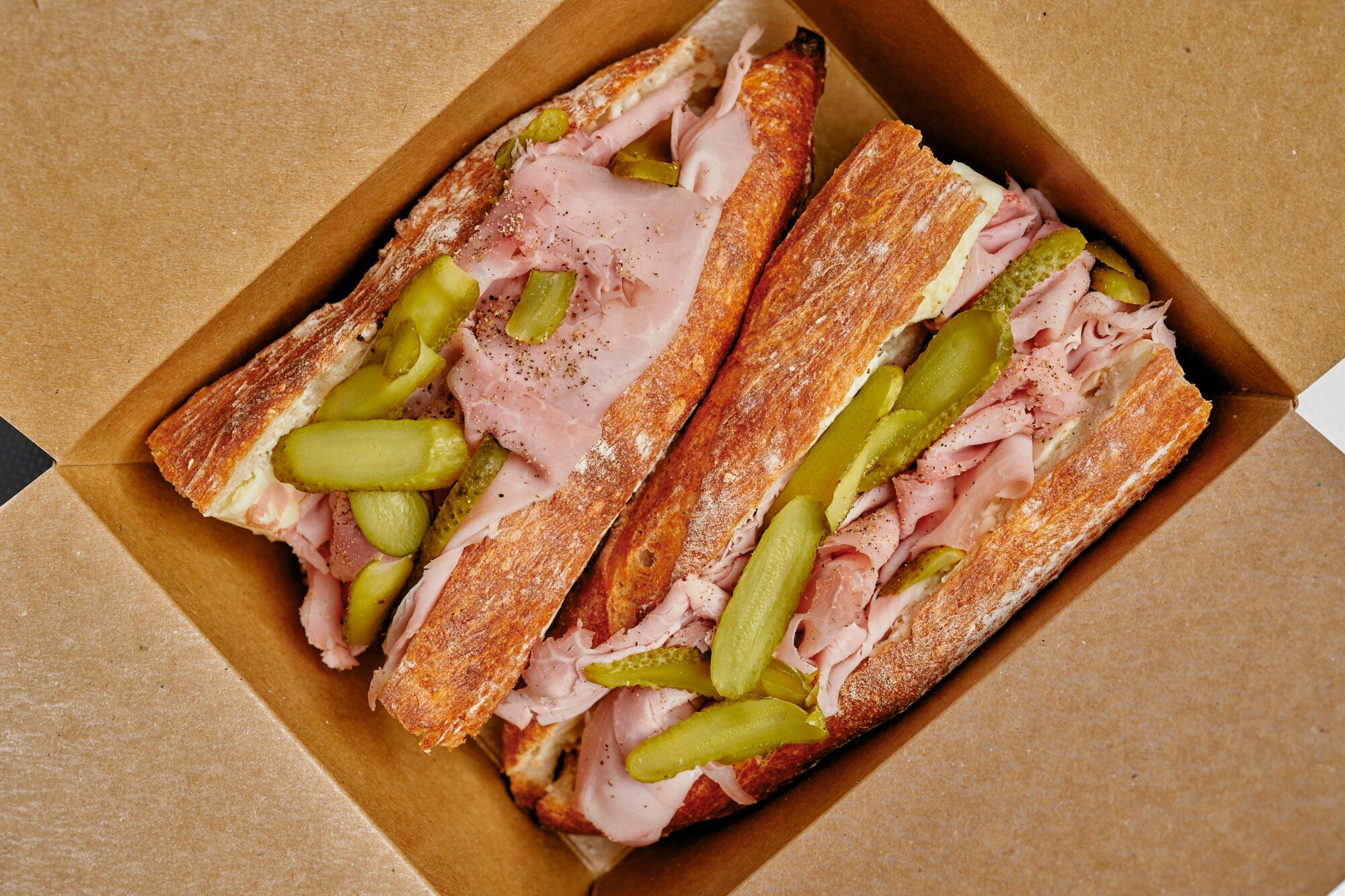 A jambon beurre sandwich on a baguette, cut in half and seen from overhead in a cardboard box
