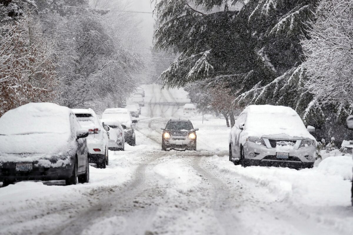 In this Feb. 11, 2019, photo, snow piles up on a street as a car maneuvers down the street in Seattle. As snow and cold temperatures hit much of the U.S, it’s time to start thinking about whether your car’s tires will get you safely through the winter. (AP Photo/Elaine Thompson, File)