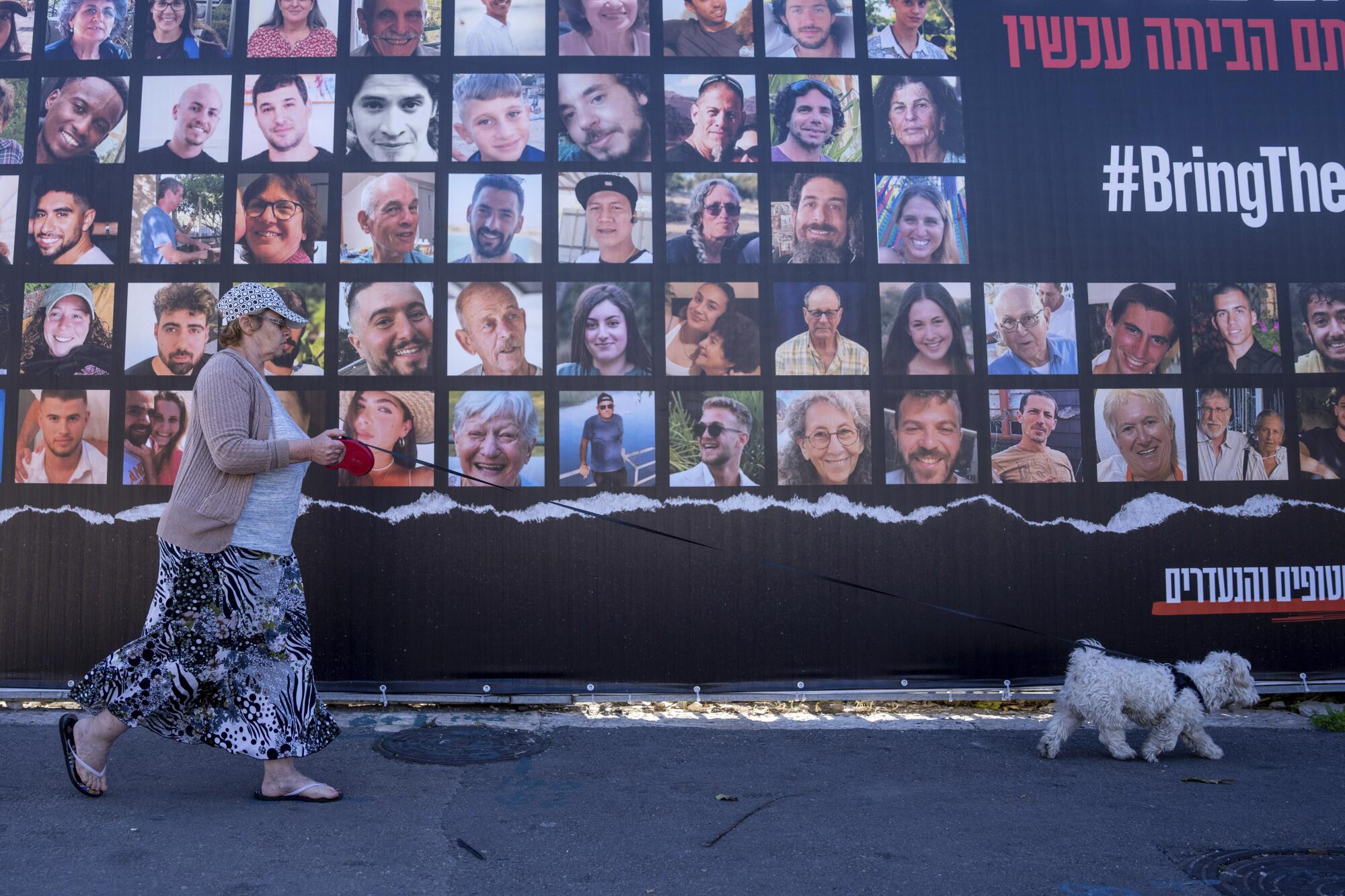 Woman walking past wall with photos of hostages held in Gaza