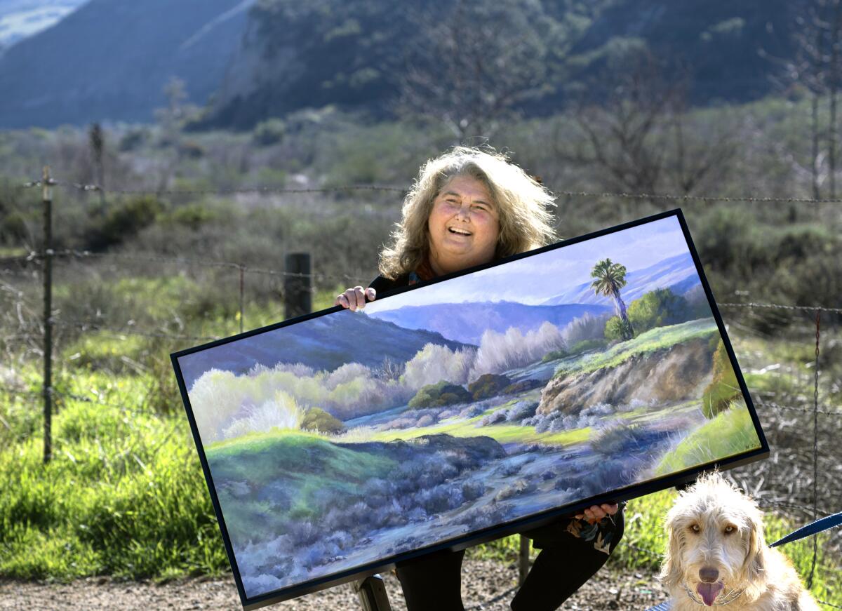 Plein air painter Monica Edwards holds a painting in a rural area of Orange County.  