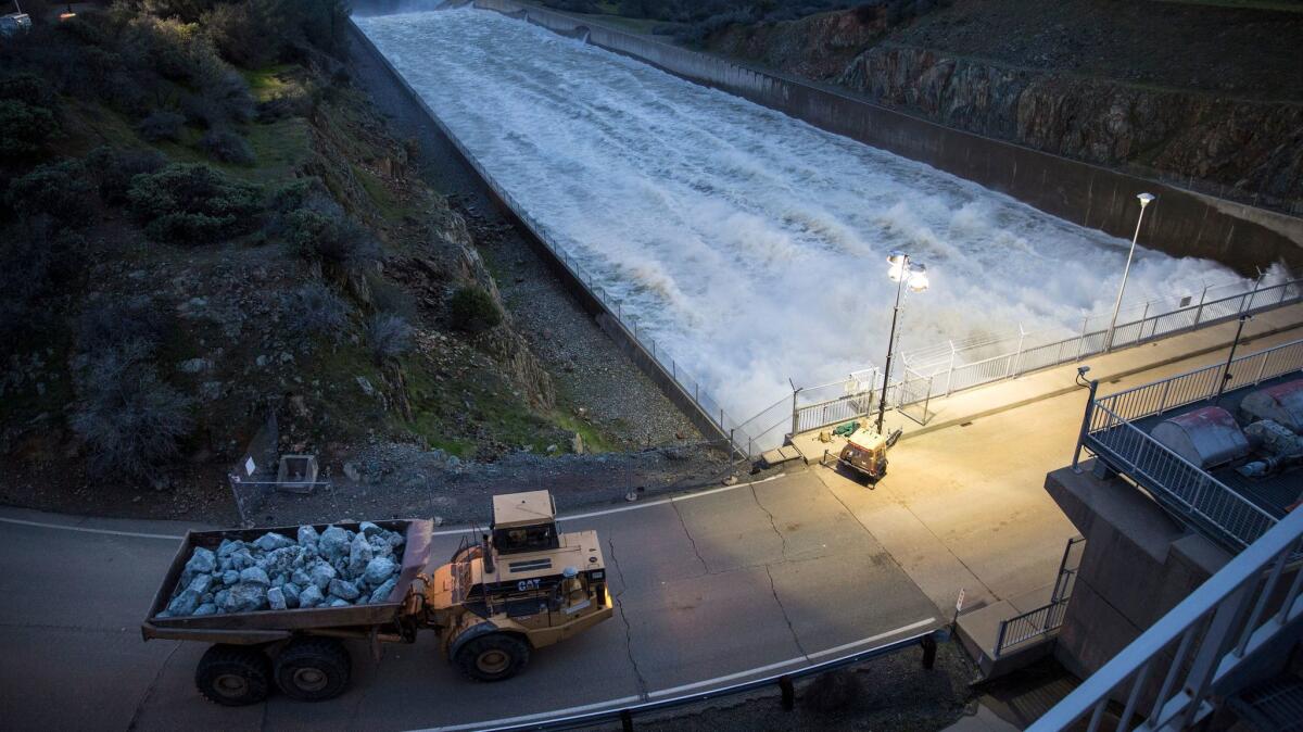 Trucks carry boulders to be used to plug eroded holes in the hillside next to Lake Oroville.