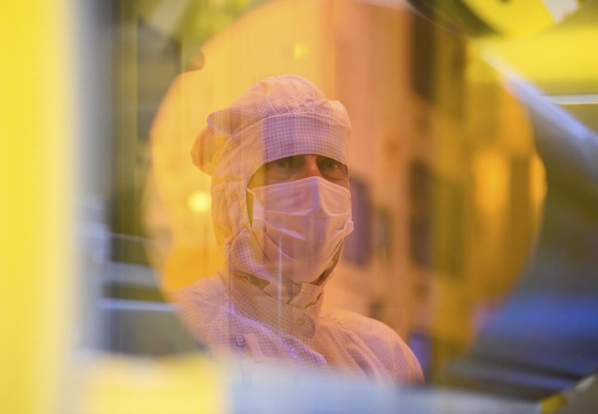 An associate is reflected in a 300-millimeter wafer in the clean room during a press tour of the new semiconductor factory of the Bosch company in Dresden, Germany, May 31, 2021. The chip factory will officially start working on June 7, 2021. (Robert Michael/dpa via AP)