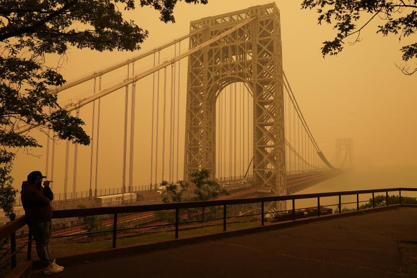 A man talks on his phone as he looks through the haze at the George Washington Bridge in Fort Lee, N.J., Wednesday, June 7, 2023. Intense Canadian wildfires are blanketing the northeastern U.S. in a dystopian haze, turning the air acrid, the sky yellowish gray and prompting warnings for vulnerable populations to stay inside. (AP Photo/Seth Wenig)