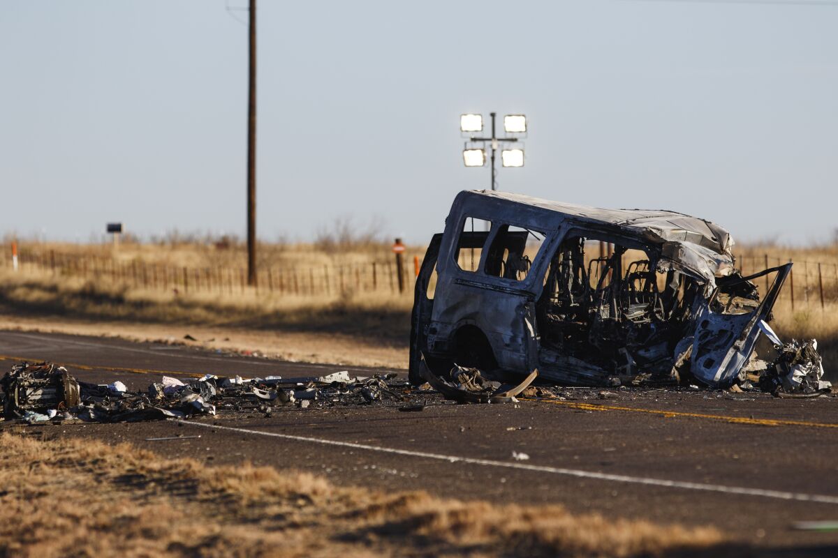 The burned-out shell of a van on a highway surrounded by debris
