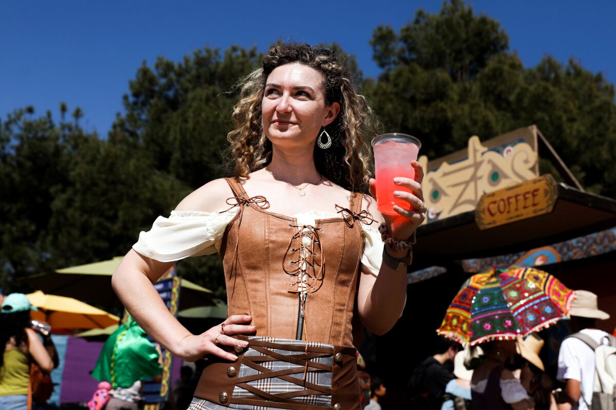 A woman wearing a leather bodice holds a pinkish-red beverage.