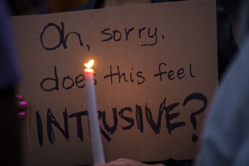 A protester holds a lighted candle in front of a sign that says "Oh, sorry, does this feel intrusive?"