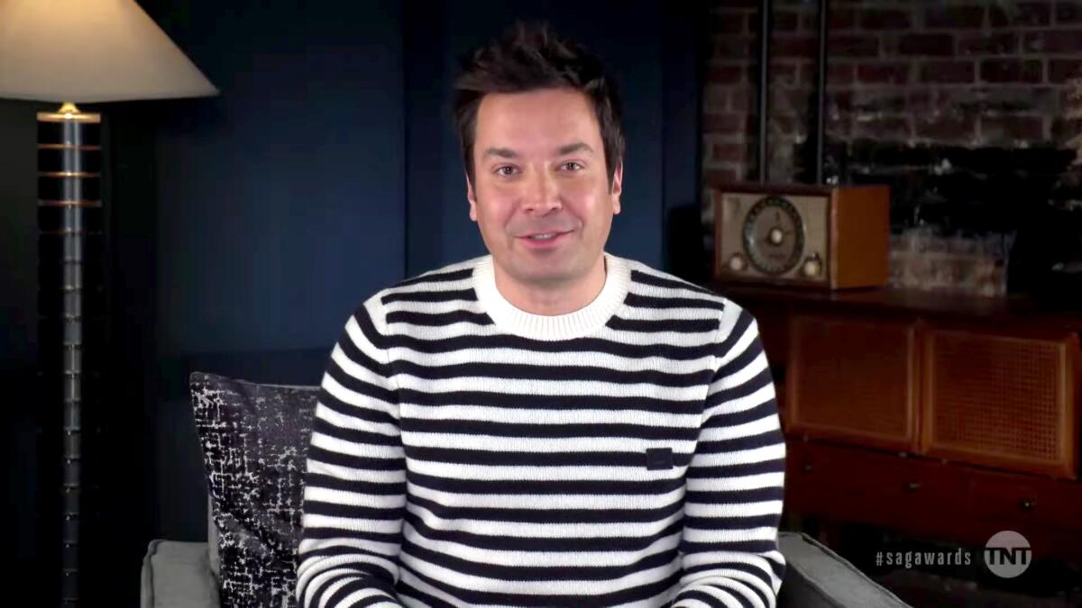 Jimmy Fallon, in a striped shirt, speaks to a camera