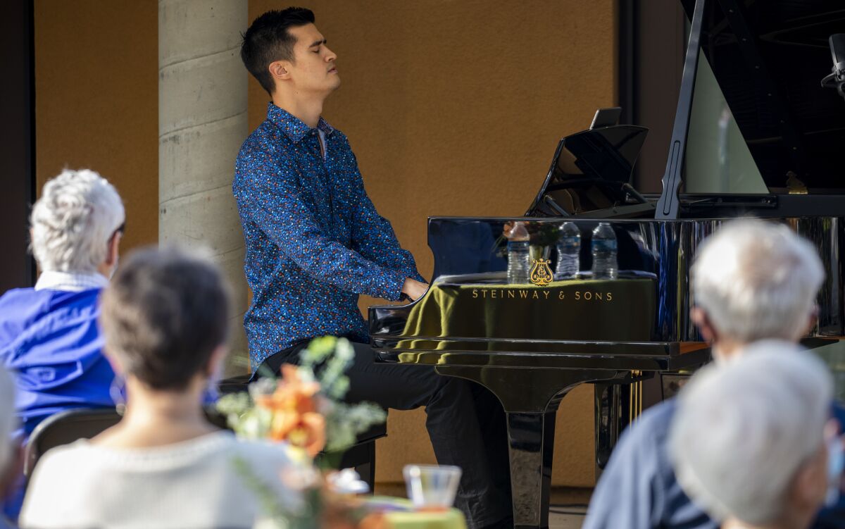 Pianist Thomas Kotcheff, in a blue shirt, plays a baby grand piano on an outdoor patio.