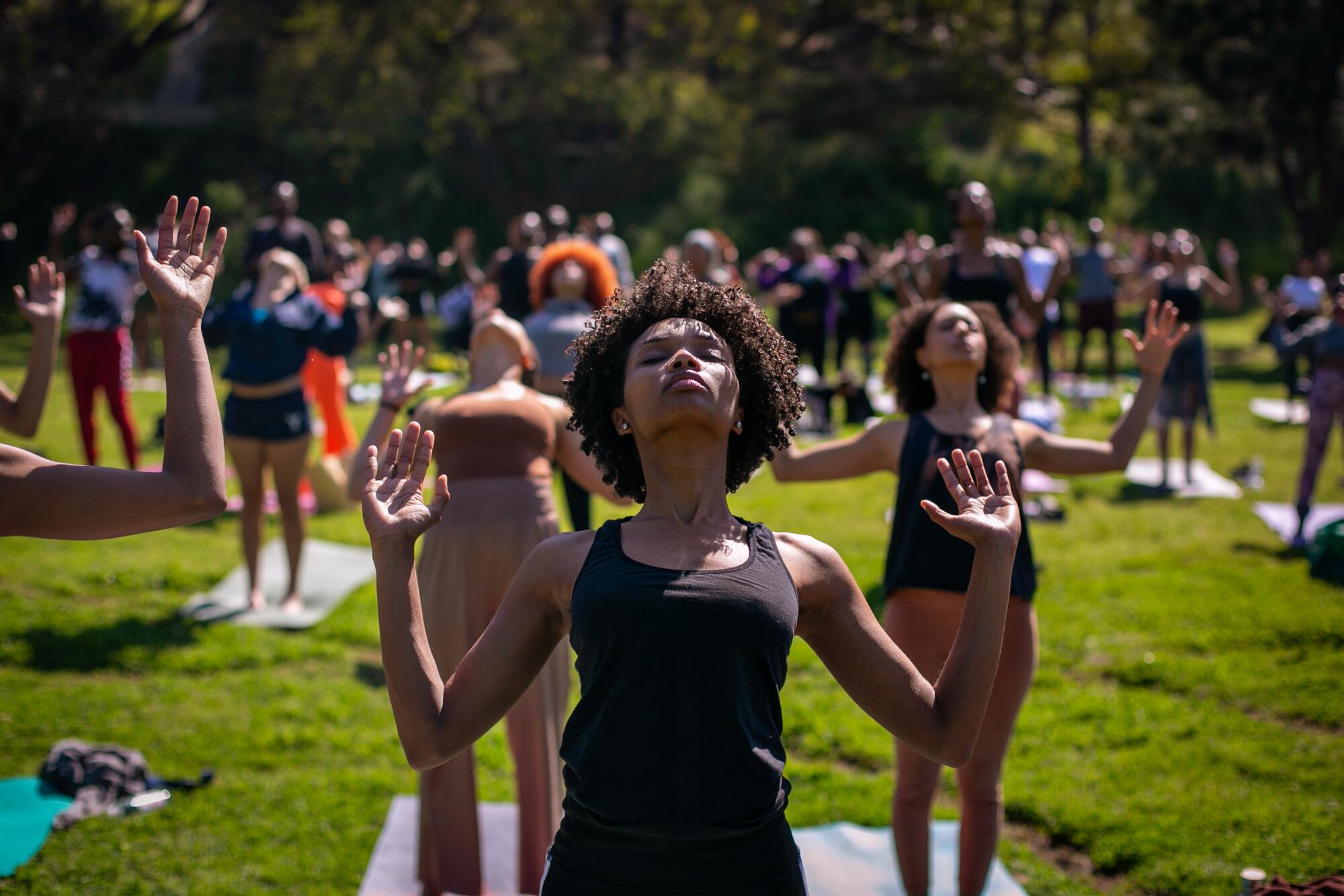 Around 200 community members raise their arms and close their eyes during yoga in a park