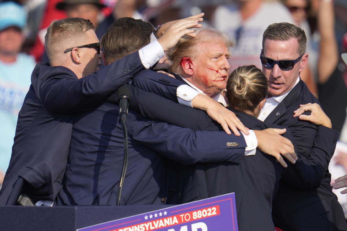 Donald Trump, with a bloody ear, is surrounded by Secret Service agents.