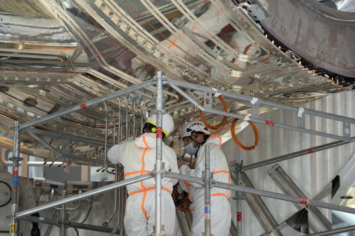 Workers in white clean suits inspect components of the International Thermonuclear Experimental Reactor