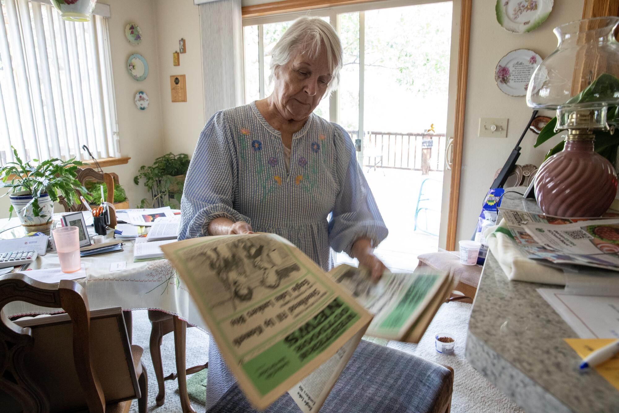 A woman looks at newspaper in a dining area.