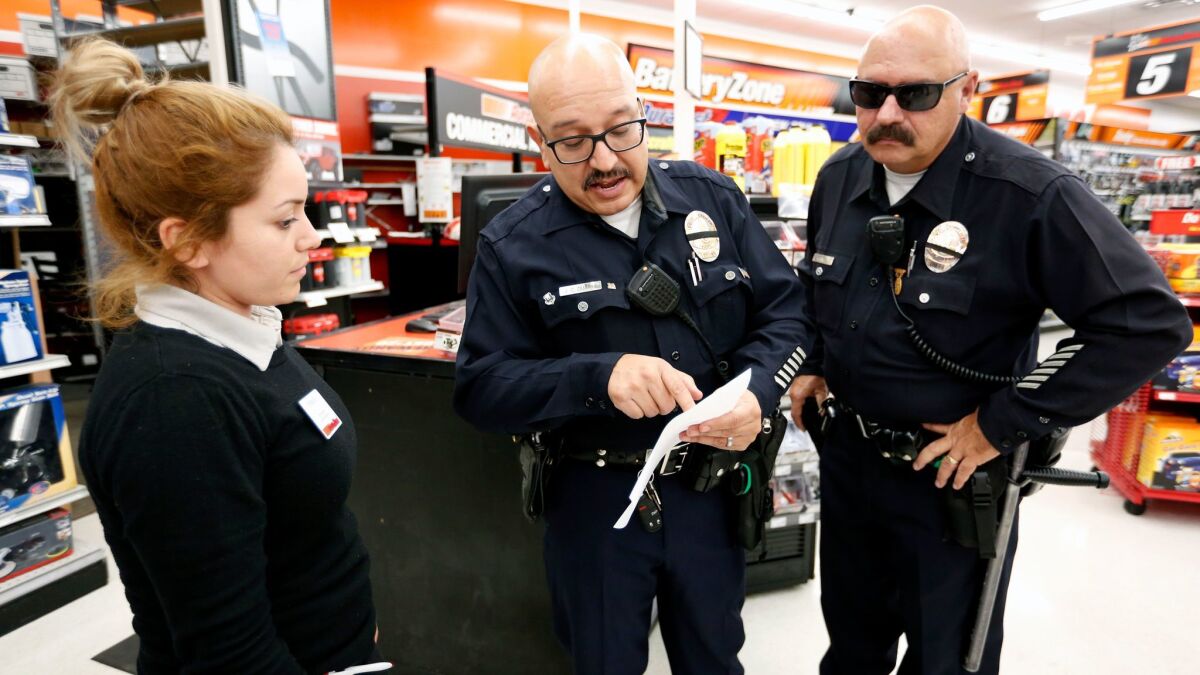 LAPD officers J.C. Duarte, center, and Harold Marinelli follow up on a stolen automobile at the AutoZone in Los Angeles with manager Brenda Olivarez.