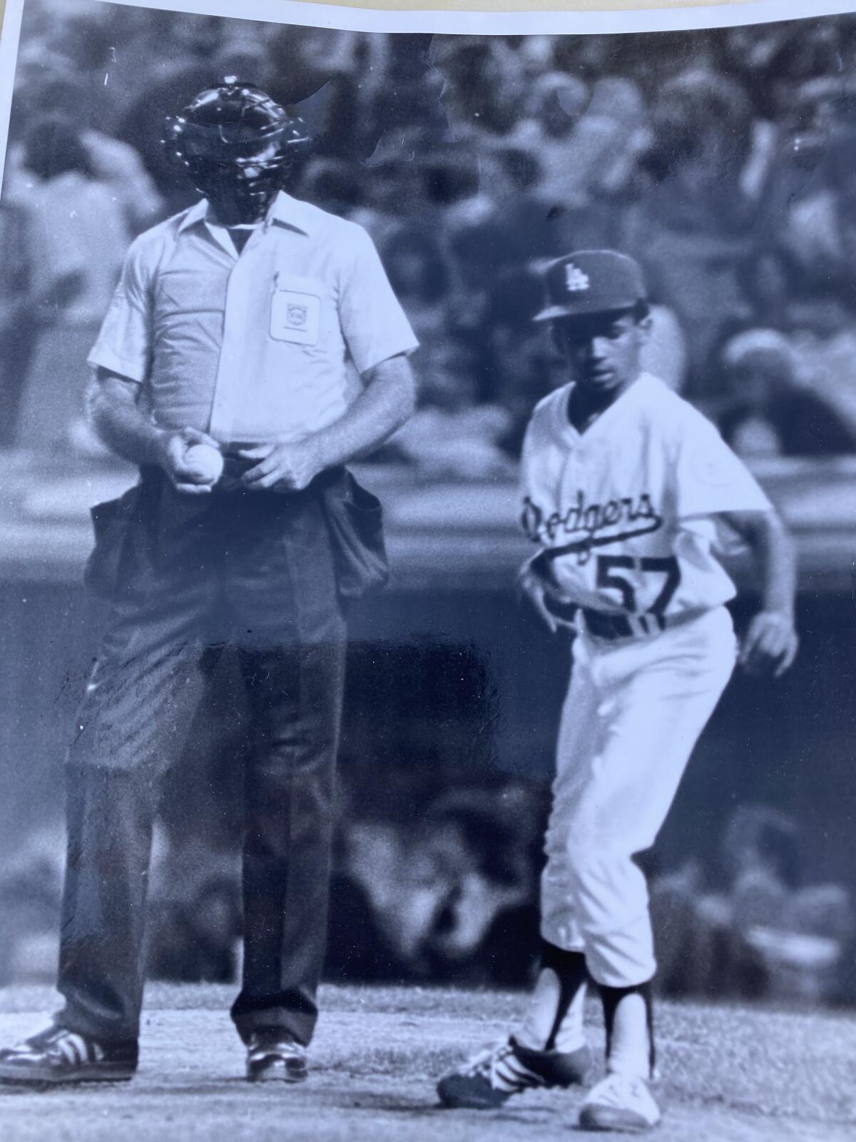 A boy in a Dodgers uniform stands next to an umpire on the field.