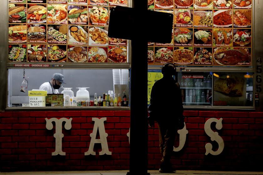 A restaurant worker completes a takeout order for a customer at a taco stand along Redondo Beach Boulevard in Hermosa Beach. Southern California has been in coronavirus lock down for about a month.