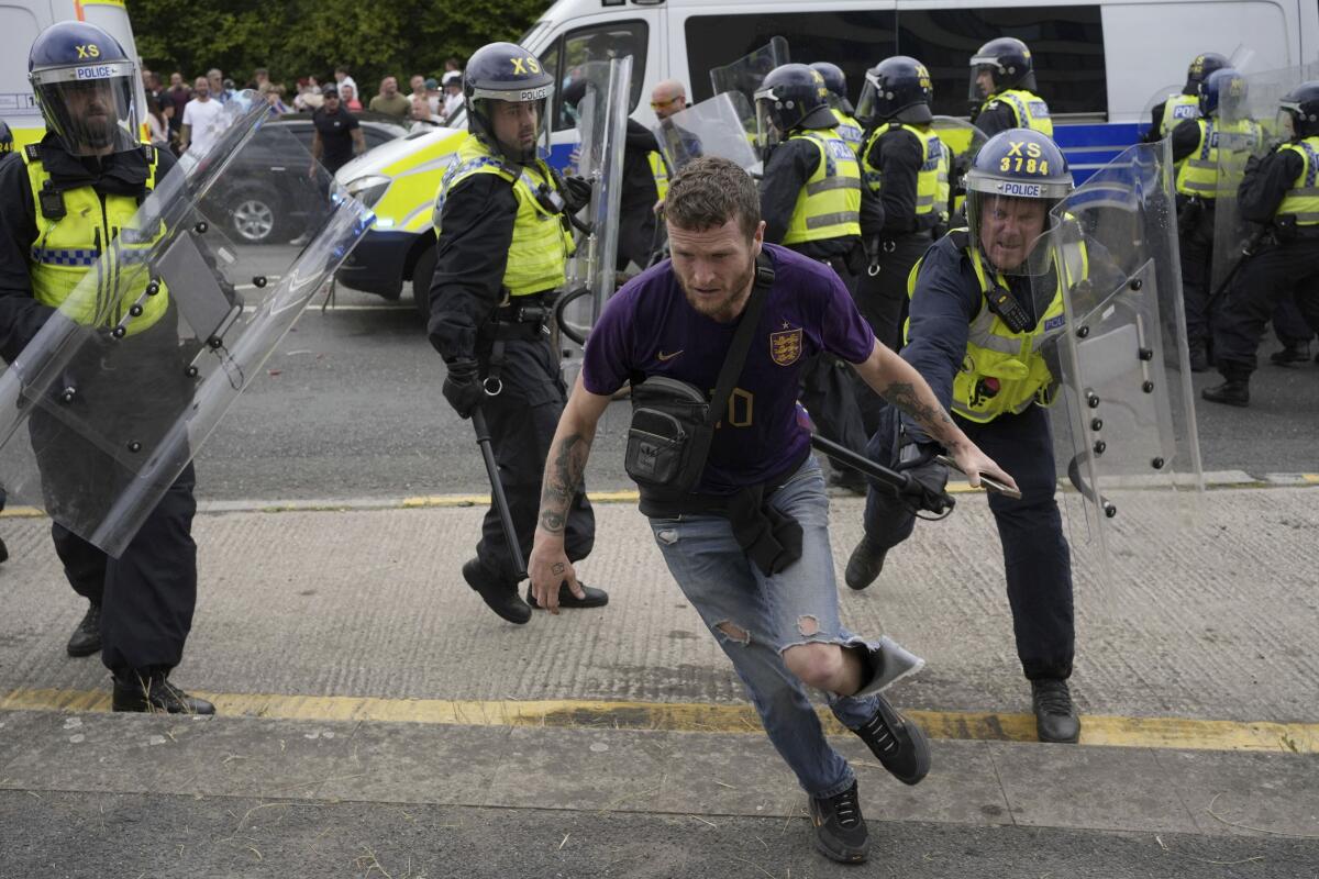 Police with helmets and clear shields chase a protester in a street