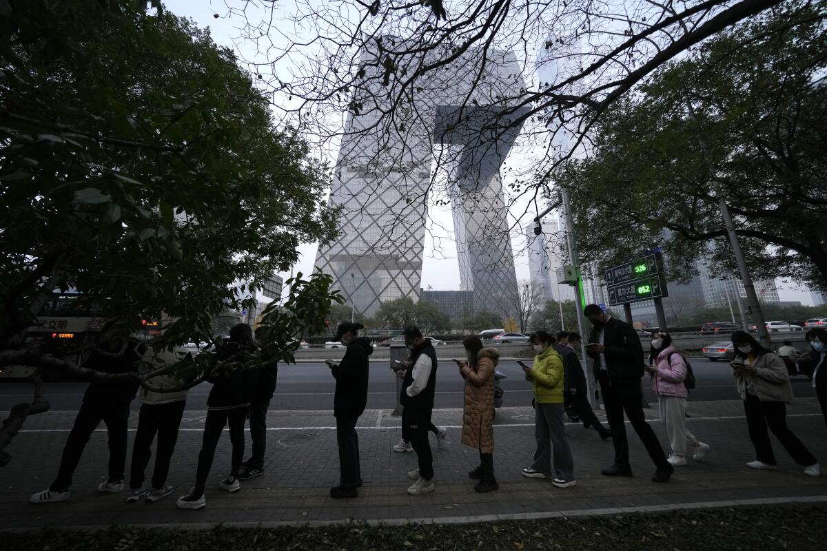 People wearing masks line up for coronavirus tests near a tower.