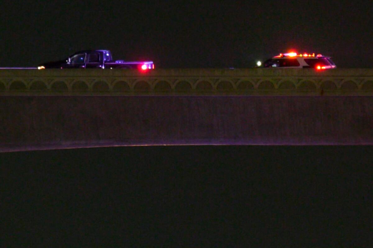 Two vehicles are parked on a freeway overpass at night.